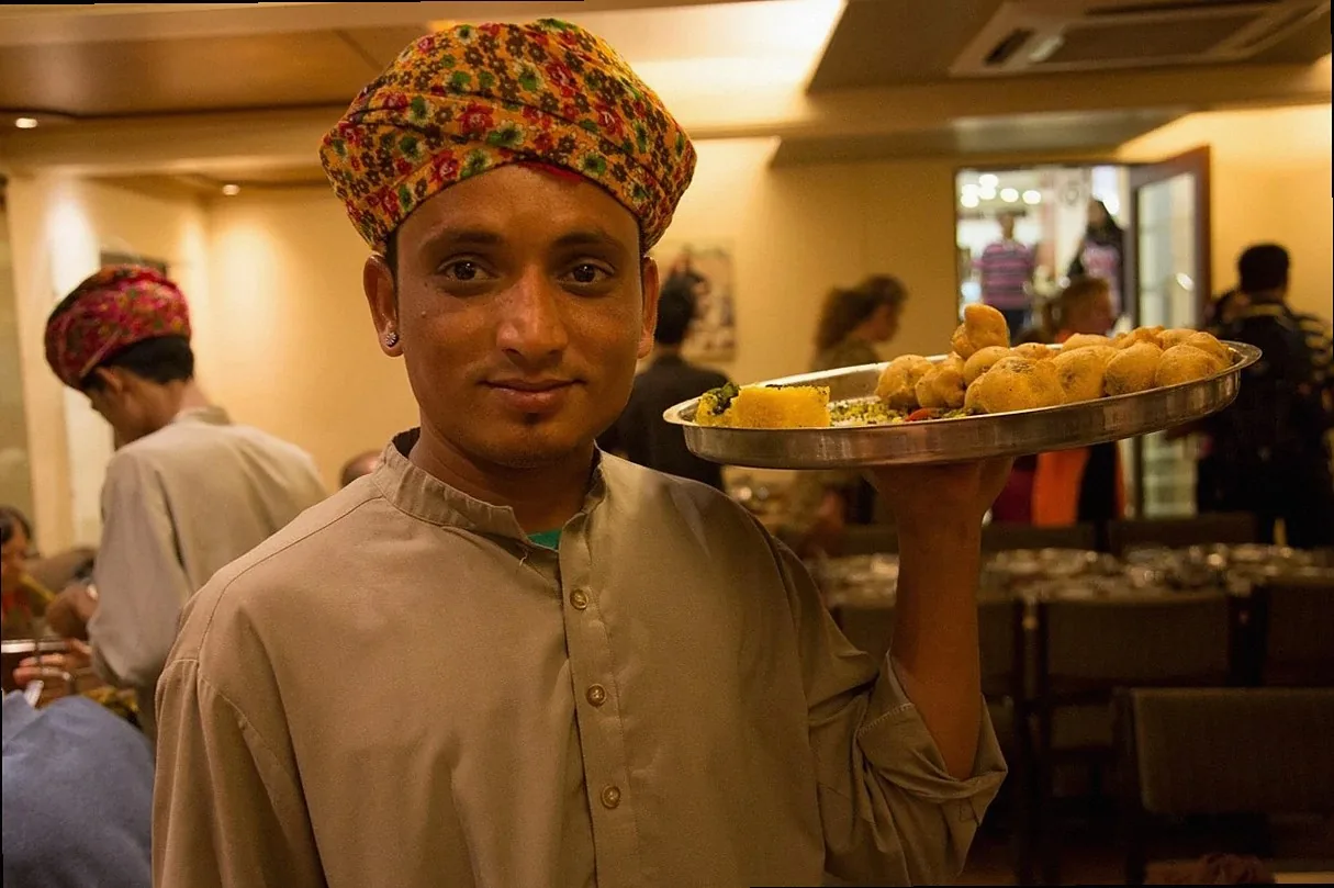 インドの若いアジア人男性ウェイターがレストランで料理を持ち、笑顔でサービスを提供している
